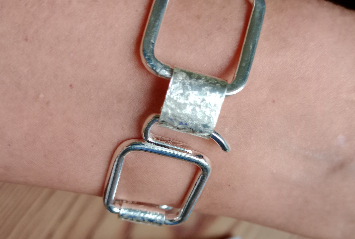 Close-up of a silver belt buckle on a wrist against a neutral background