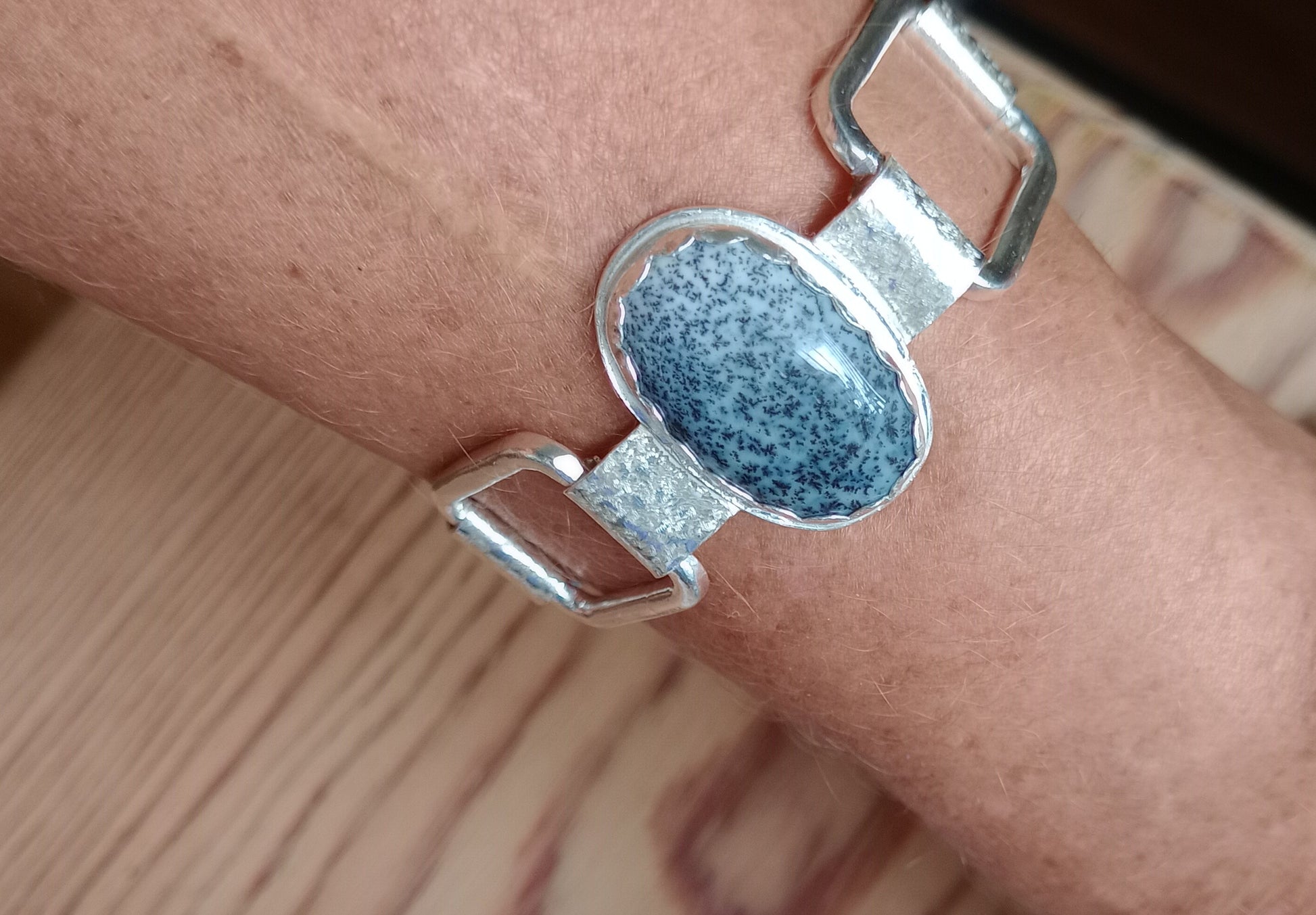 Silver bracelet with a blue speckled stone on a wrist against a wooden surface.