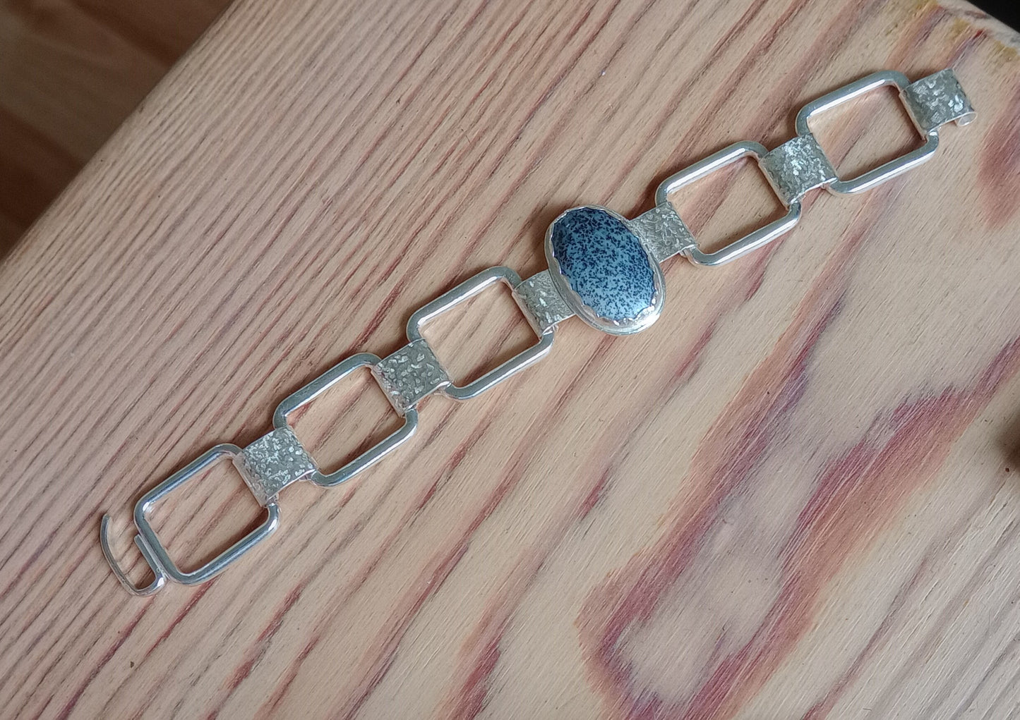 Silver bracelet with a central blue stone on a wooden surface